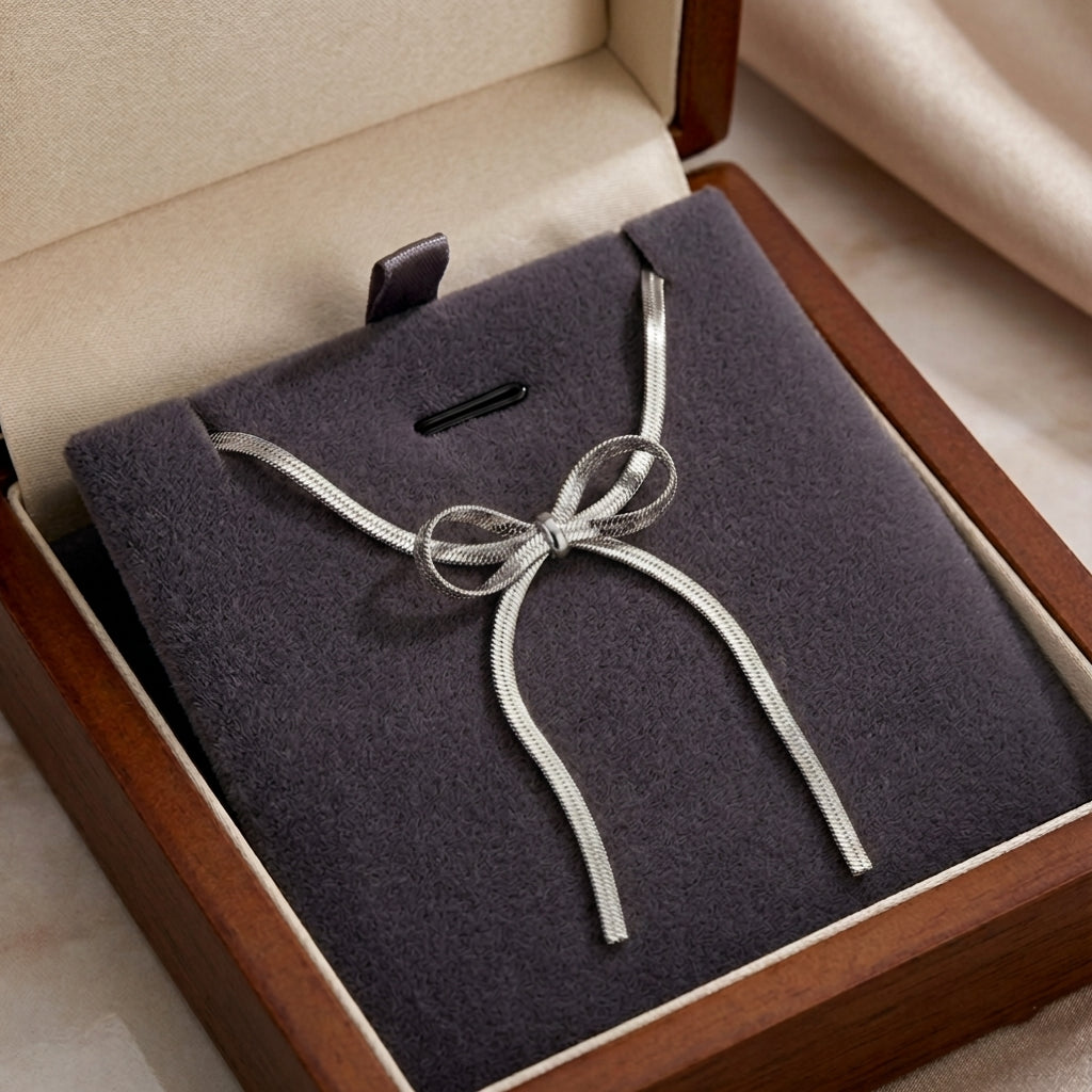 Le collier nœud argenté Izia Enlacé soigneusement présenté à l'intérieur de son écrin de luxe en bois et velours gris.