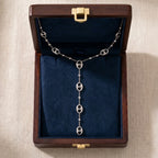 Vue de dessus d'un écrin en bois foncé ouvert avec un intérieur en velours bleu roi profond. Le collier lariat en argent Léonor Éblouissante est soigneusement disposé à l'intérieur, mettant en valeur son design et ses maillons argentés.