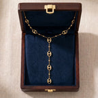 Vue de dessus d'un écrin en bois foncé ouvert avec un intérieur en velours bleu roi profond. Le collier lariat doré Léonor Éblouissante est soigneusement disposé à l'intérieur, mettant en valeur son design et ses maillons argentés.
