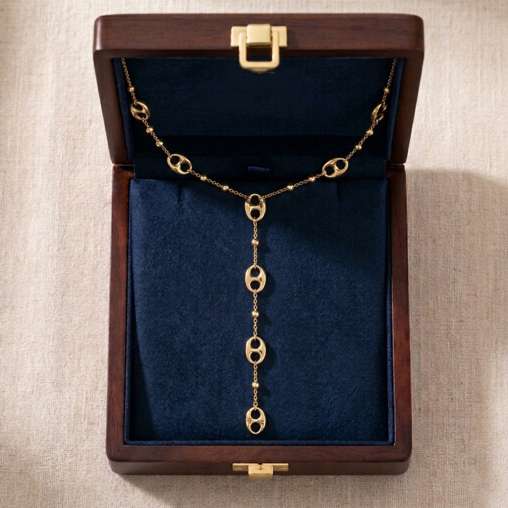 Vue de dessus d'un écrin en bois foncé ouvert avec un intérieur en velours bleu roi profond. Le collier lariat doré Léonor Éblouissante est soigneusement disposé à l'intérieur, mettant en valeur son design et ses maillons argentés.