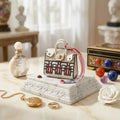 Micro-sac bijou Écrin Haussmannien en cuir blanc albâtre avec motifs architecturaux noirs et cordon Twilly rose, présenté sur un socle en marbre blanc