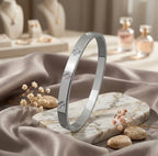 Bracelet jonc en argent poli Alix Distinguée présenté debout sur un socle en marbre blanc veiné de gris, entouré de fleurs séchées et galets