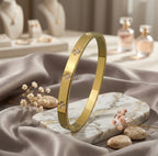 Bracelet jonc en or poli Alix Distinguée présenté debout sur un socle en marbre blanc veiné de gris, entouré de fleurs séchées et galets