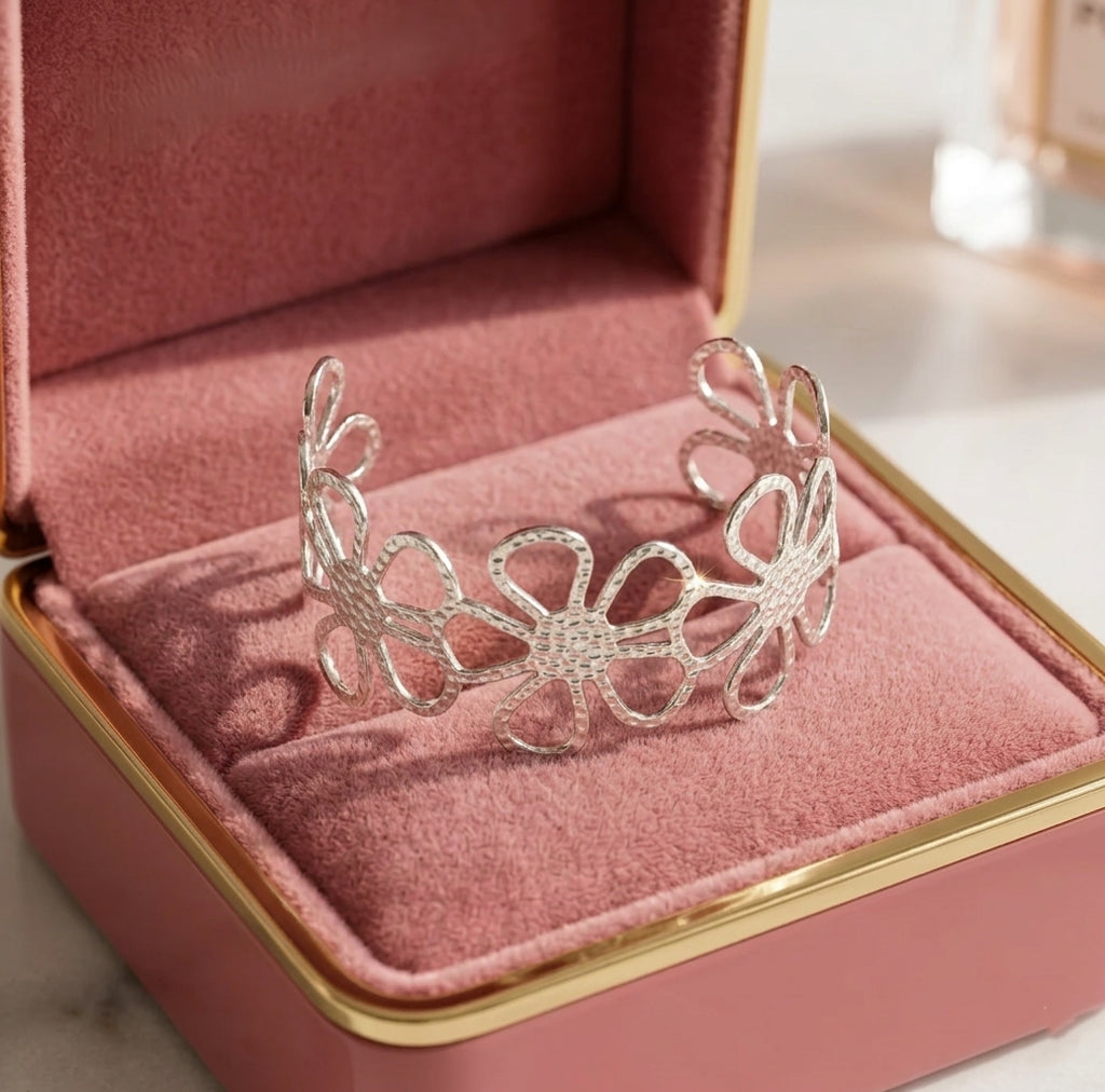 Jonc doré Flora Éclatante au motif de fleurs ajourées, présenté dans un écrin de luxe en velours rose poudré avec finitions argentées.