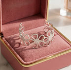 Jonc doré Flora Éclatante au motif de fleurs ajourées, présenté dans un écrin de luxe en velours rose poudré avec finitions argentées.