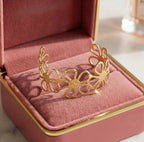 Jonc doré Flora Éclatante au motif de fleurs ajourées, présenté dans un écrin de luxe en velours rose poudré avec finitions dorées.