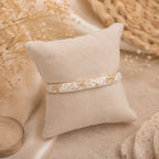 Bracelet jonc thaïlandais Sakura blanc nacré présenté sur un coussin en tissu écru.