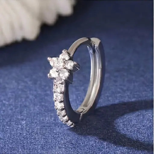 Gros plan détaillé sur une mini-créole huggie Iris de Maison Dosana en acier inoxydable doré, ornée d'un motif floral pavé d'oxydes de zirconium brillants.