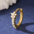 Gros plan détaillé sur une mini-créole huggie Iris de Maison Dosana en acier inoxydable doré, ornée d'un motif floral pavé d'oxydes de zirconium brillants.