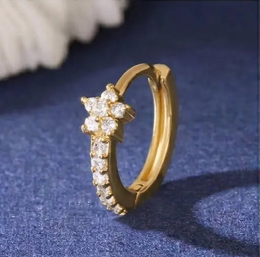 Gros plan détaillé sur une mini-créole huggie Iris de Maison Dosana en acier inoxydable doré, ornée d'un motif floral pavé d'oxydes de zirconium brillants.