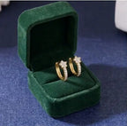 Une paire de mini-créoles Iris en acier inoxydable doré et zircons, présentées dans un écrin de luxe en velours vert émeraude ouvert.