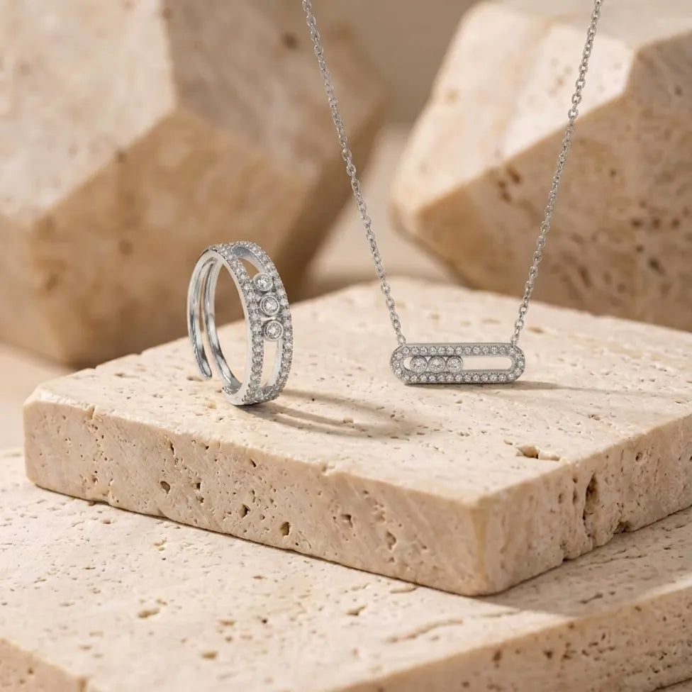Bijoux en acier inoxydable argenté Sacha l'Instinctive présentés sur un bloc de pierre travertin, design moderne avec trois zircons.