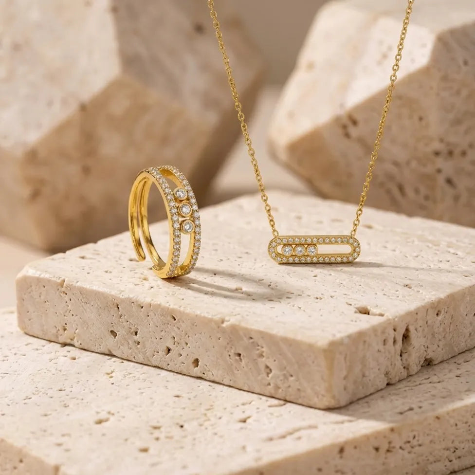 Bijoux en acier inoxydable doré Sacha l'Instinctive présentés sur un bloc de pierre travertin, design moderne avec trois zircons.