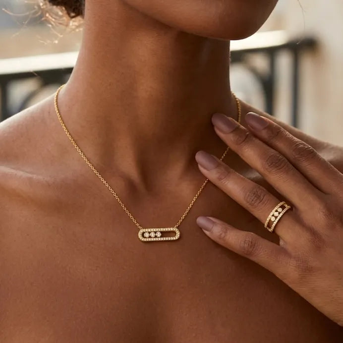 Parure Sacha l'Instinctive dorée portée par une femme comprenant un collier avec pendentif rectangulaire et une bague ajustable assortie, tous deux sertis de trois zircons.